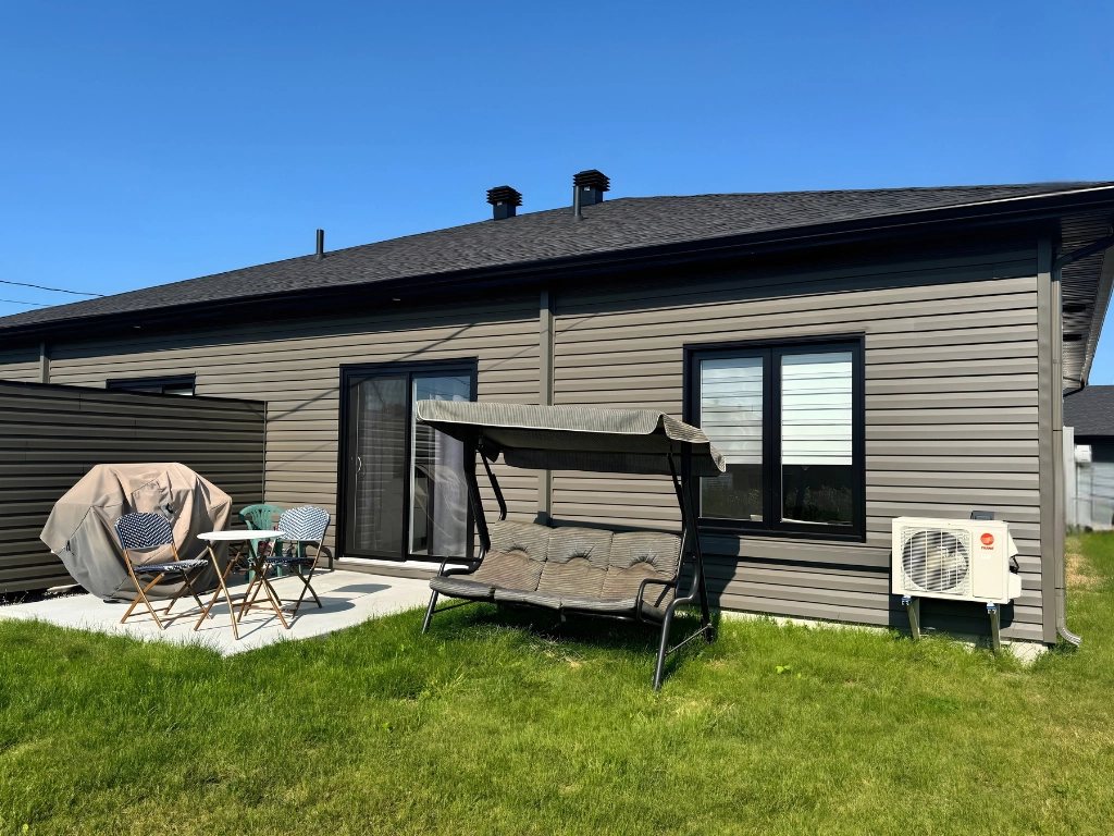 Cour arrière privée d'une résidence pour aînés aux Résidences Haziel — terrasse béton, pelouse verte, thermopompe et mobilier extérieur